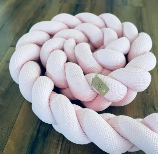Gespielte rosa Nestchenschlange aus geflochtenem Material, perfekte Bettschlange für sicheren und stilvollen Babyschlaf.
