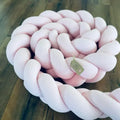 Gespielte rosa Nestchenschlange aus geflochtenem Material, perfekte Bettschlange für sicheren und stilvollen Babyschlaf.